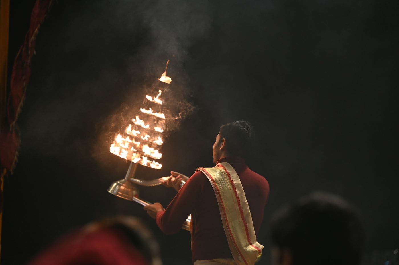 A priest raises a tiered aarti lamp full of flames during an evening ceremony