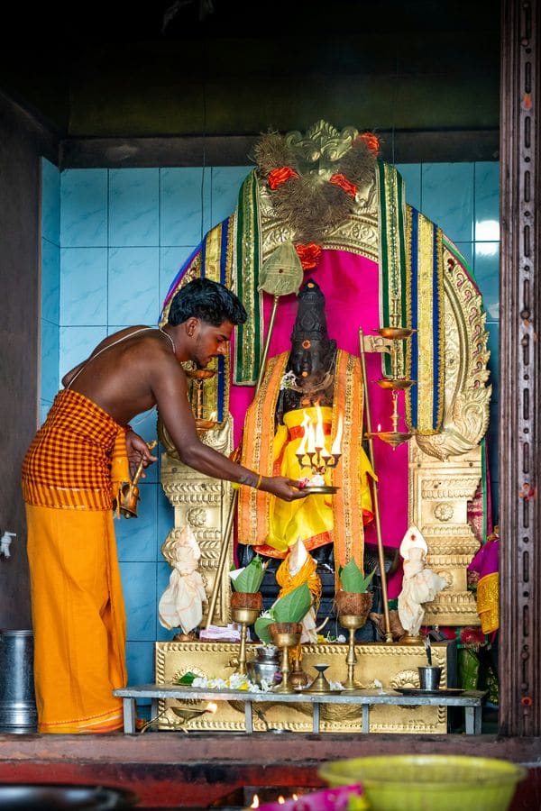 A priest offering a lamp before a decorated deity in a temple